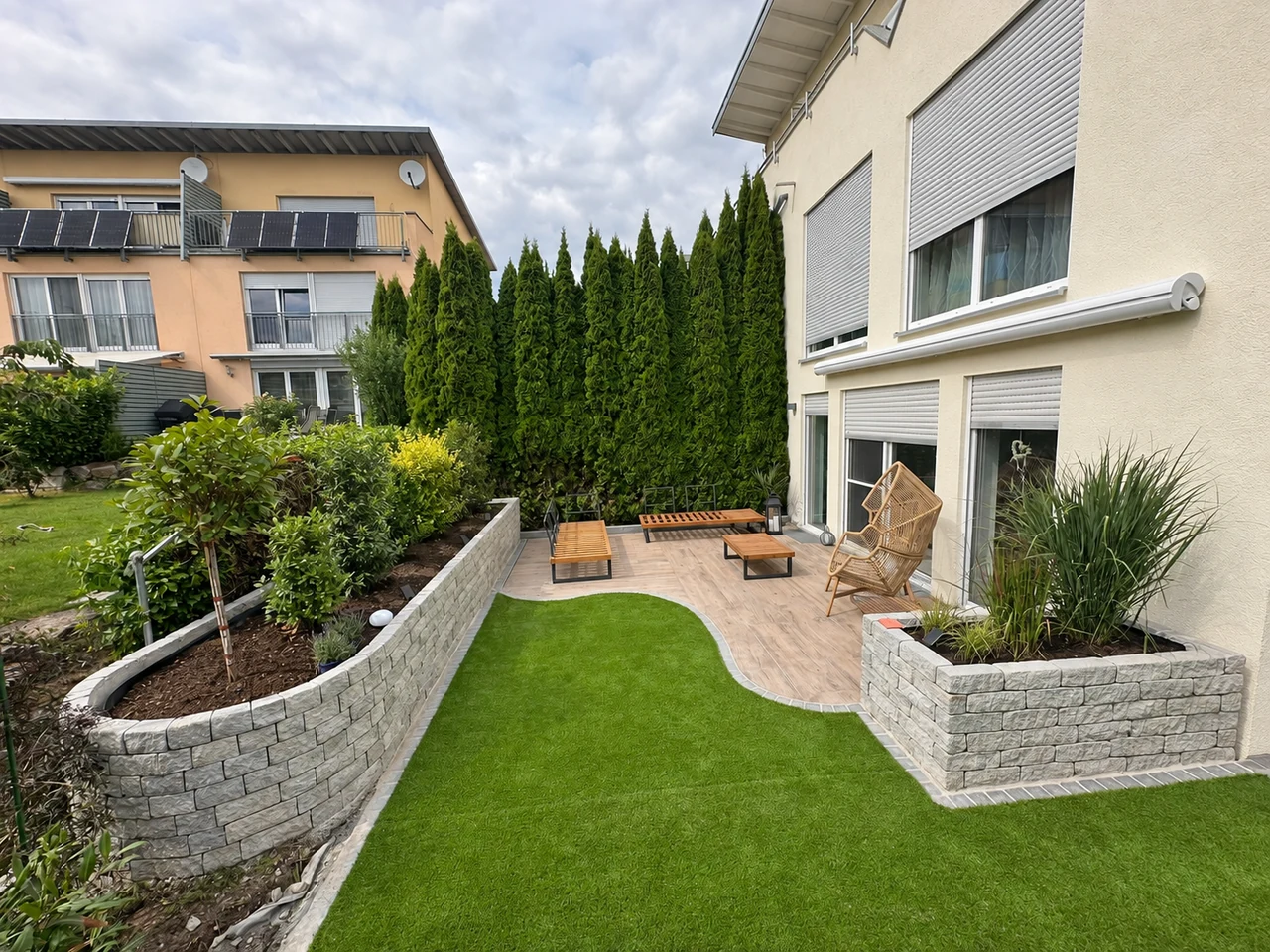 Terrasse mit geschwungenen Steinmauern, Beeten und grüner Rasenfläche